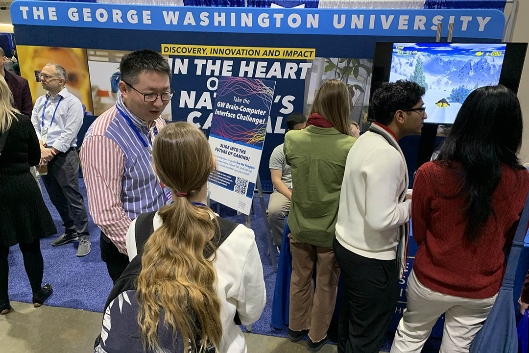 Computer Science Professor Xiaodong Qu (center) talks with visitors to GW’s booth at the 2025 AAAS annual meeting in Boston.