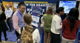 Computer Science Professor Xiaodong Qu (center) talks with visitors to GW’s booth at the 2025 AAAS annual meeting in Boston.